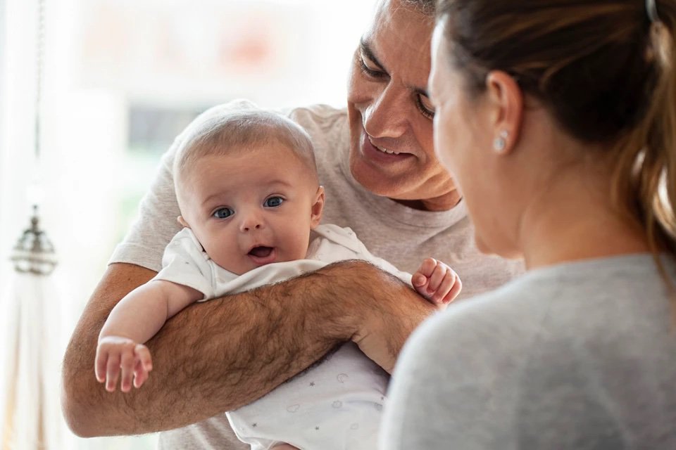 Mutter spielt mit Baby während Vater es im Arm hält