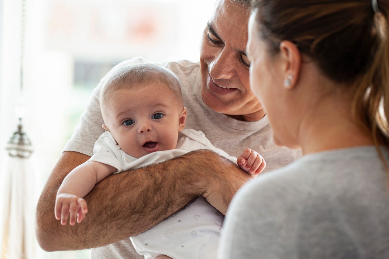 Mother playing with her baby boy while his father holding him on his arms.