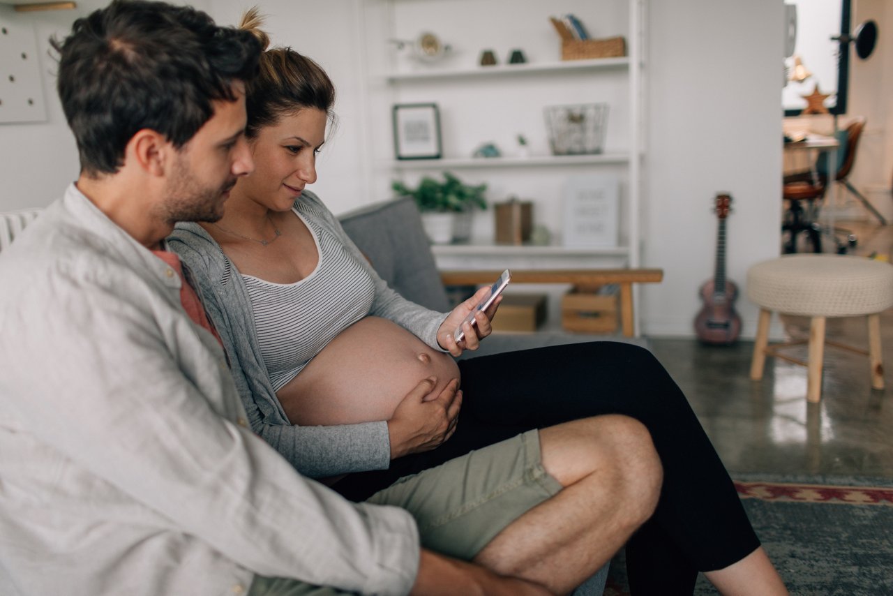 Photo of a young couple using the mobile phone to listen to the heartbeats of their unborn child