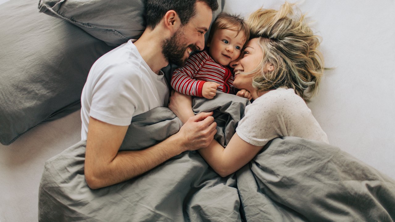 Parents cuddling with their toddler in bed