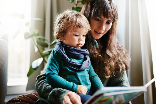 Kleinkind schaut mit Mutter ins Buch