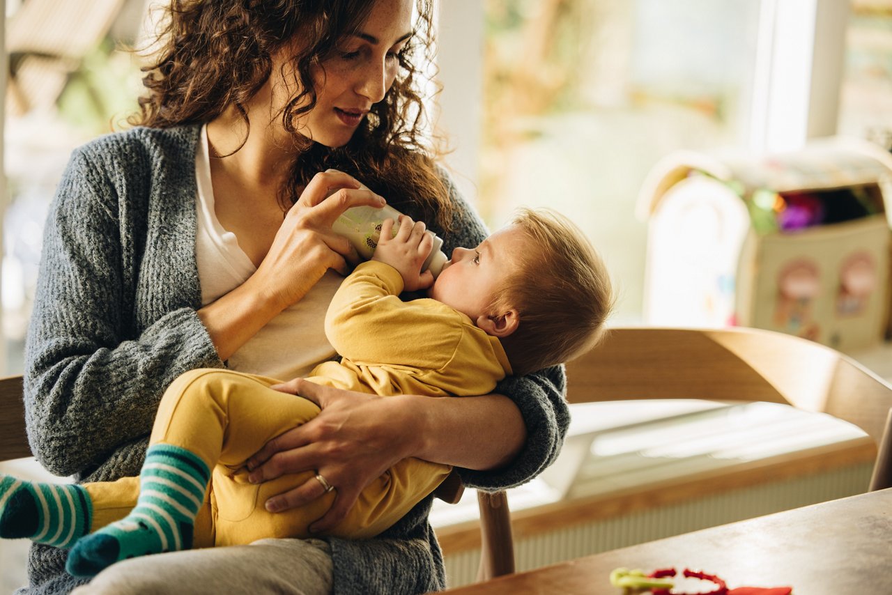 Newborn baby drinking milk from bottle. Cute toddler in mother's arms with milk bottle.
