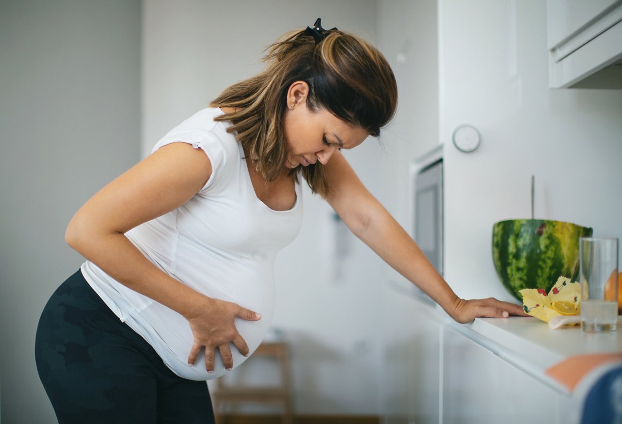 Pregnant woman is standing in the kitchen feeling contractions. She leaned against the kitchen counter to ease the pain she was feeling.