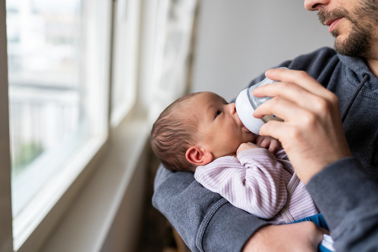 Close up of cute little baby eating milk from baby bottle,unrecognizable person feeding baby