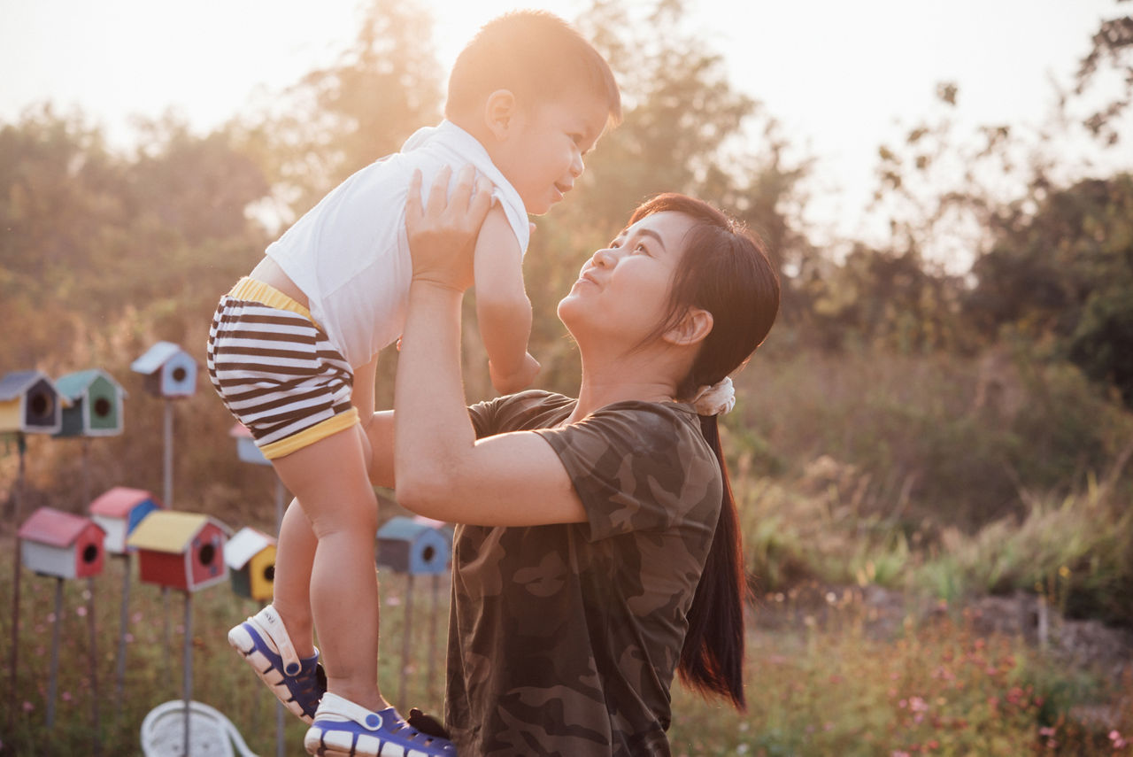 Happy young mother playing and having fun with her little baby son in the park on a sunny summer day. Family on sunset