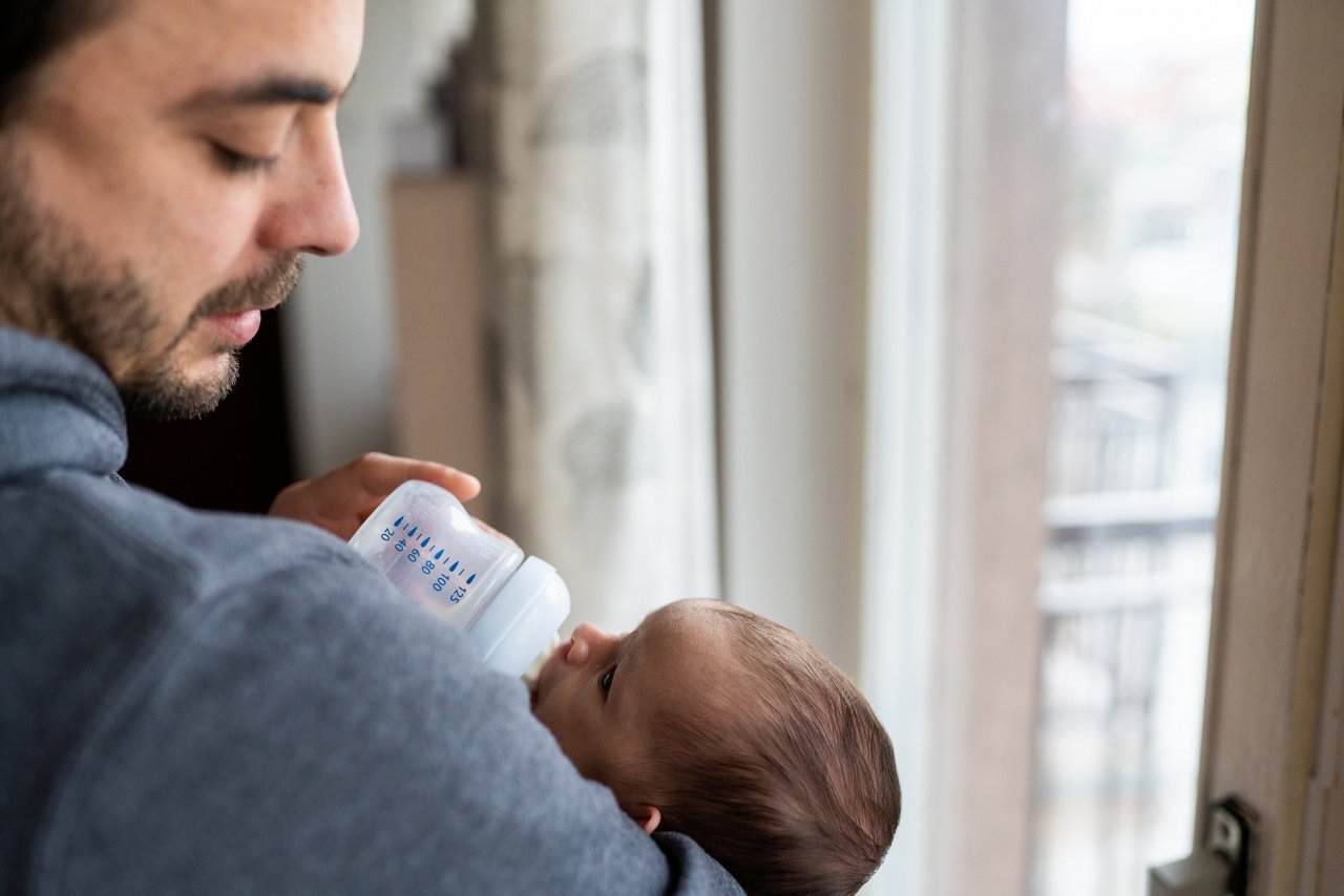 Affectionate love between father and newborn baby, father holding his son in arms, feeding baby with milk in apartment