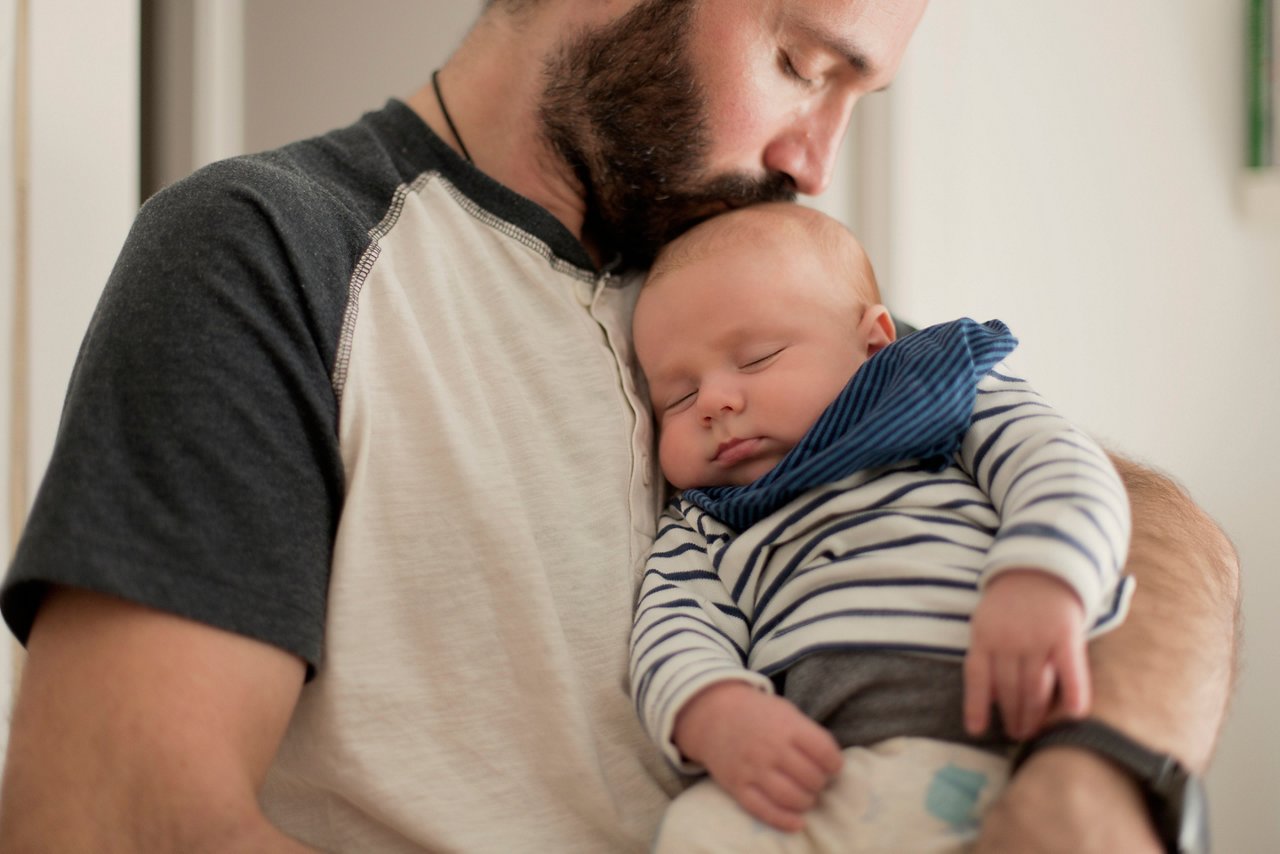 Dad is kissing his newborn baby that has fell asleep in his arms