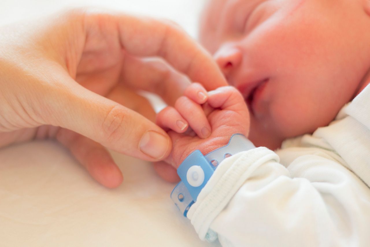 Newborn baby boy sleeping in his crib, his mother's hand holding his little hand.