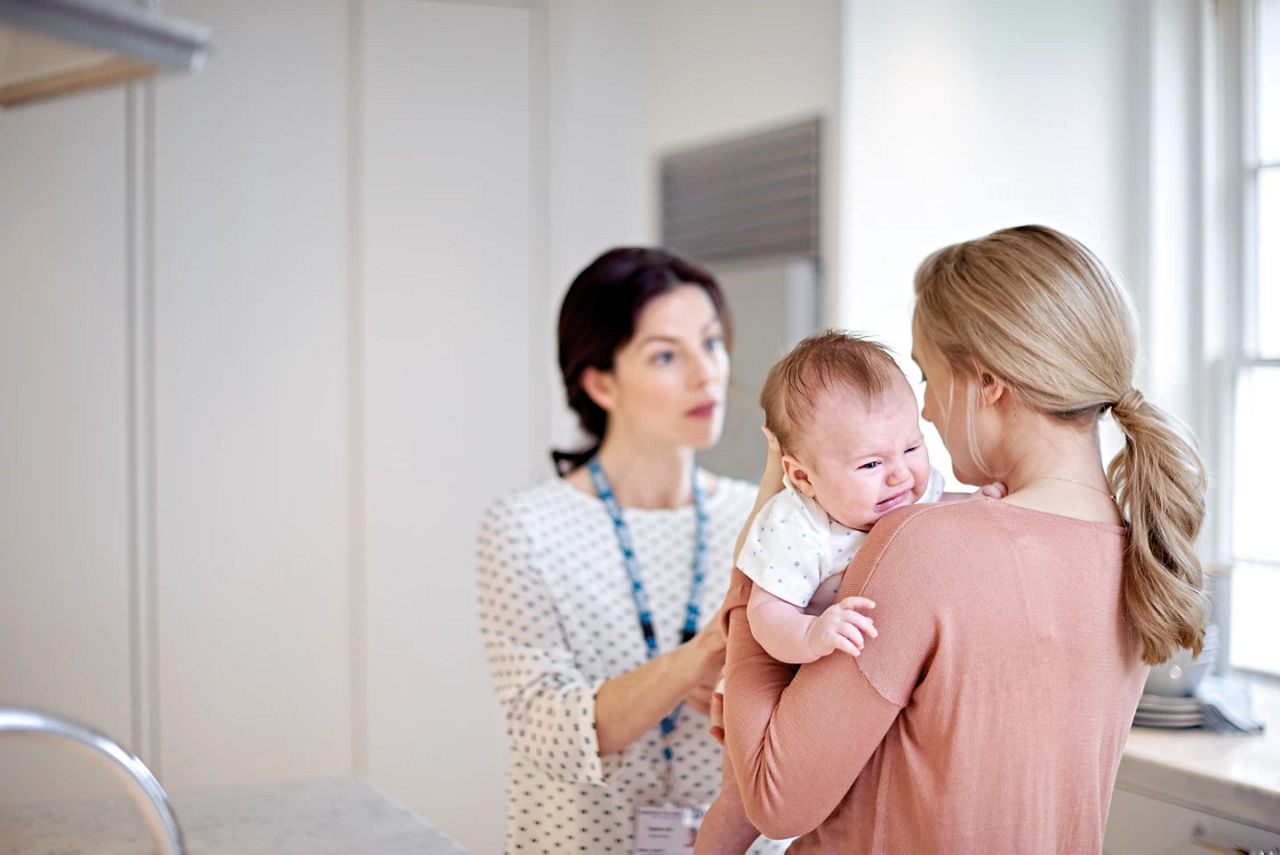 Mother holder her crying baby at the GP appointment