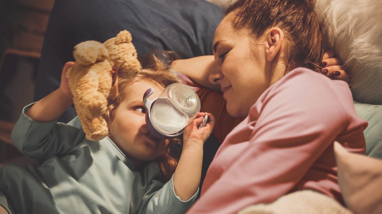 Moeder kijkt naar kindje die uit flesje drinkt