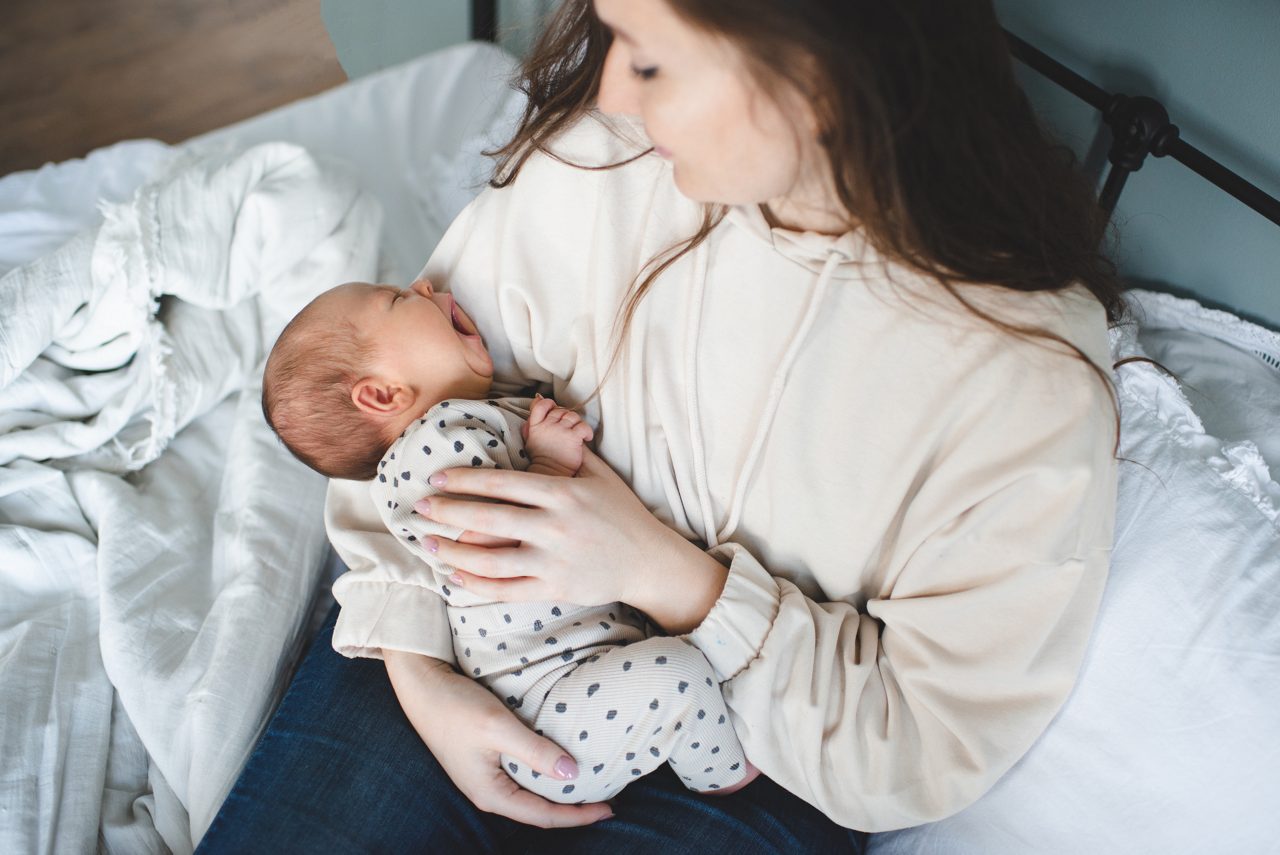 Crying baby girl on mother hands with colic stomach ache in bed. Health care. Sick infant child with woman at home. Motherhood.