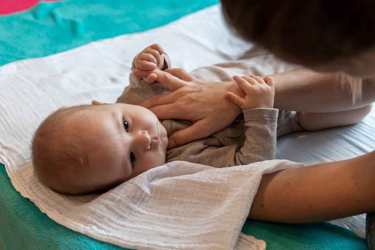 Baby liegt auf dem Rücken auf einer Decke mit einer Hand auf dem Bauch, die es festhält.