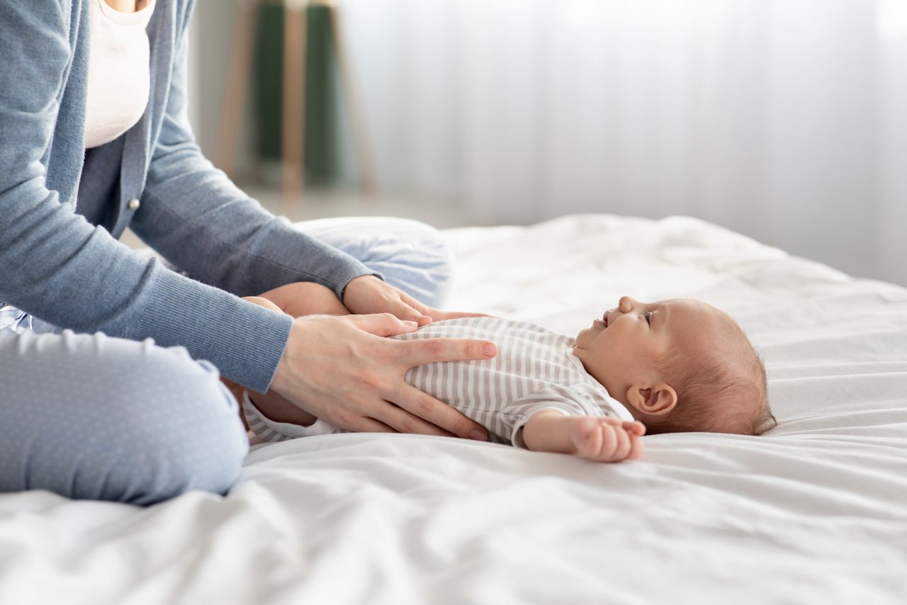 Baby liegt auf dem Rücken auf einer Decke mit einer Hand auf dem Bauch, die es festhält.