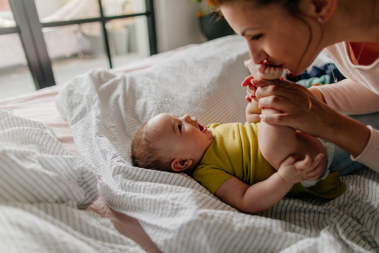 Mama mit Baby auf dem Arm steht am Fenster.