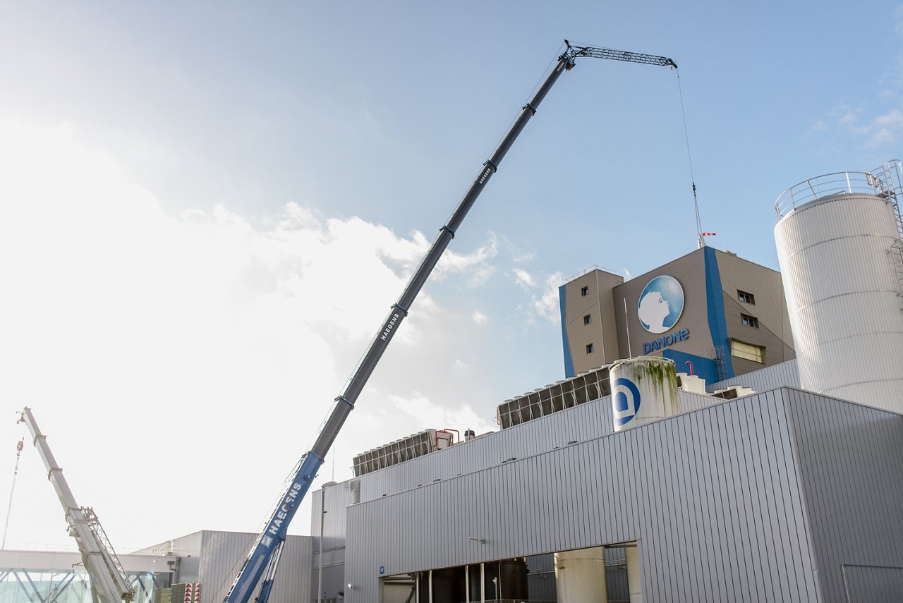 Danone-productiesite met hijskranen en industriële installaties onder een blauwe hemel.