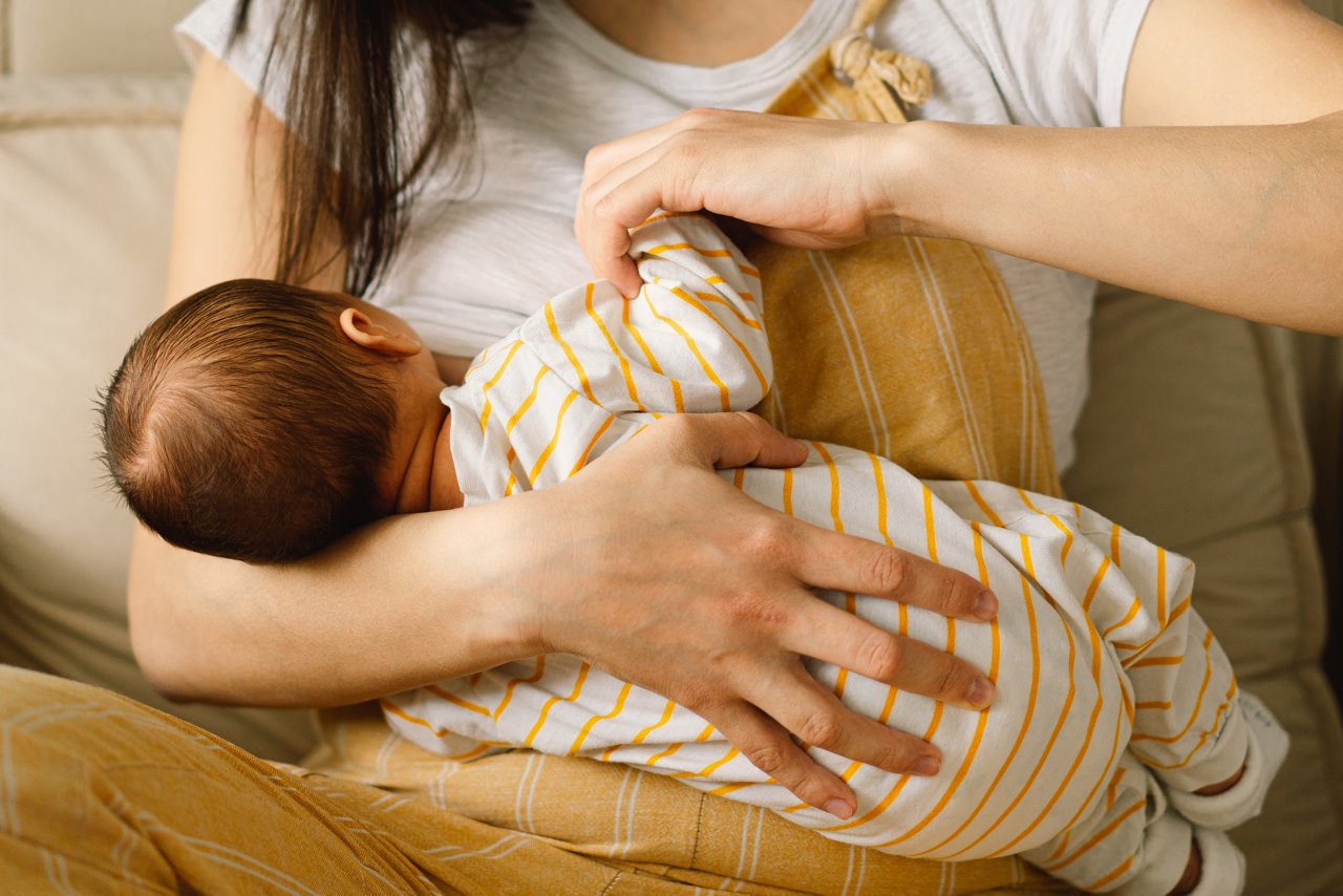 Baby beim Stillen, zwischen Kopf und Schulter der Mama hindurch zu sehen.