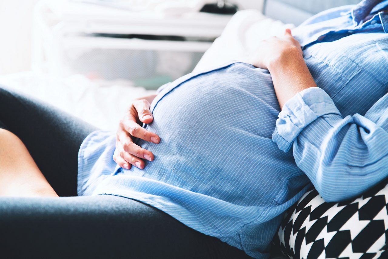 Schwangere liegt im Bett und streichelt ihren Bauch