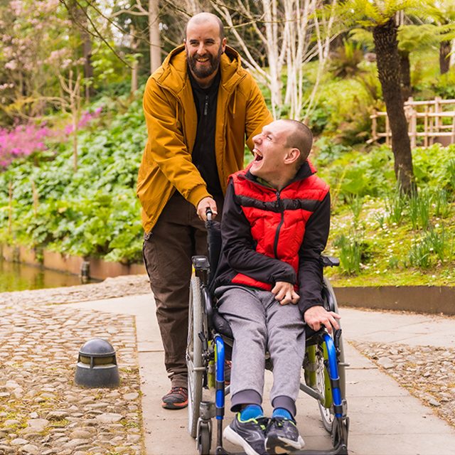 A person in a public city park in the wheelchair, walking together with a friend