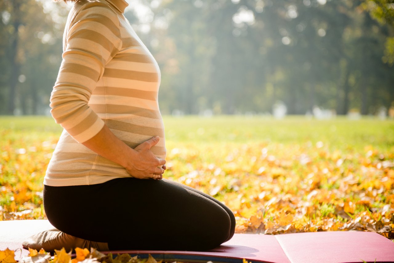 Frau hält sich Babybauch und sitzt draußen in der Natur 