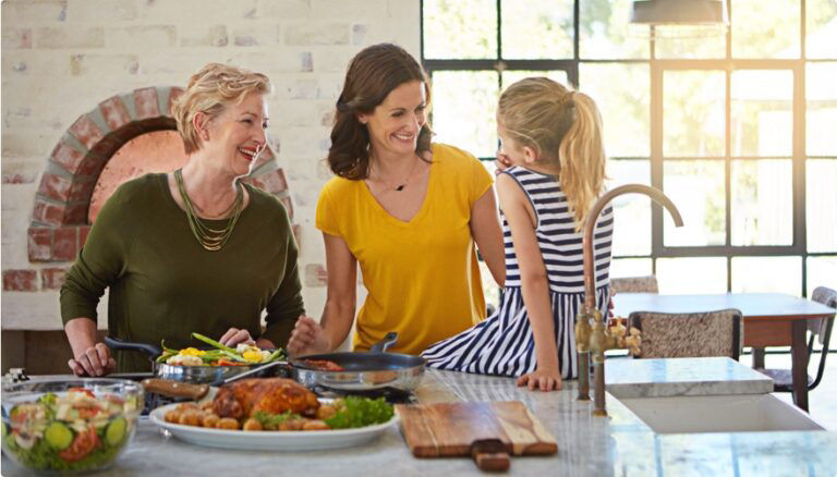 Two women looking at a girl sitting on the counter top in kitchen