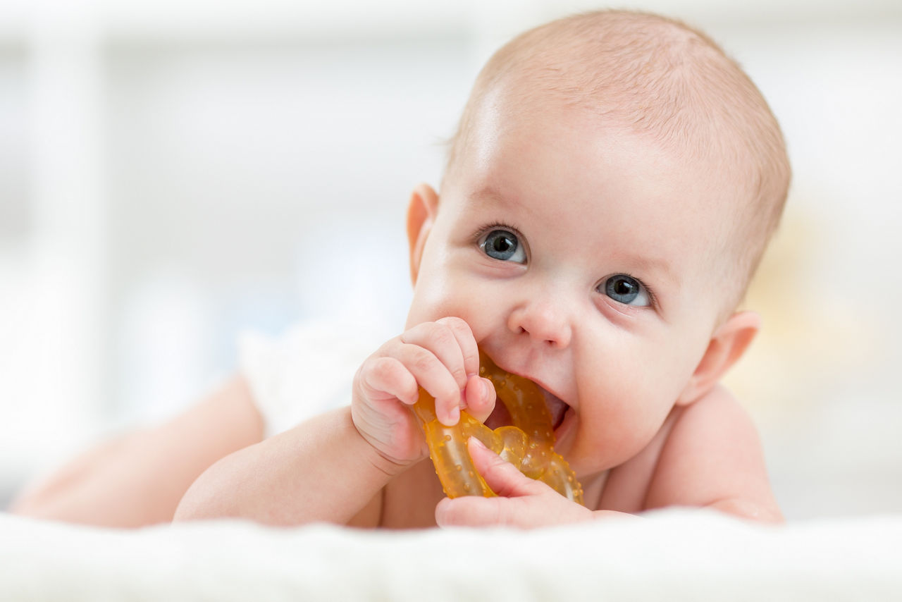 baby lying on bed using teething ring