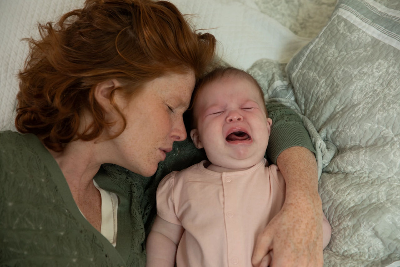 Mother hugging crying baby on bed