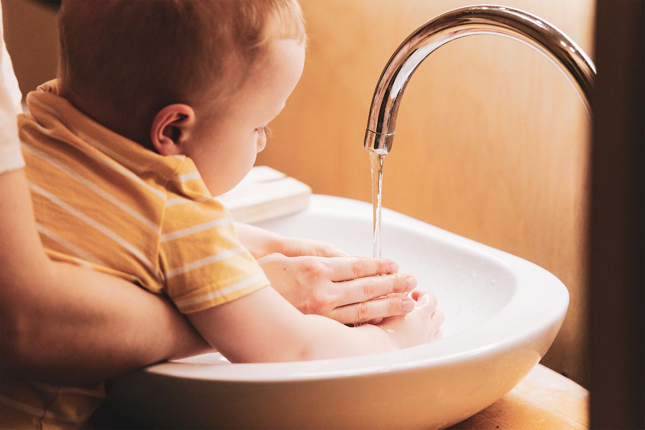 Baby hält Hände unter einen Wasserstrahl