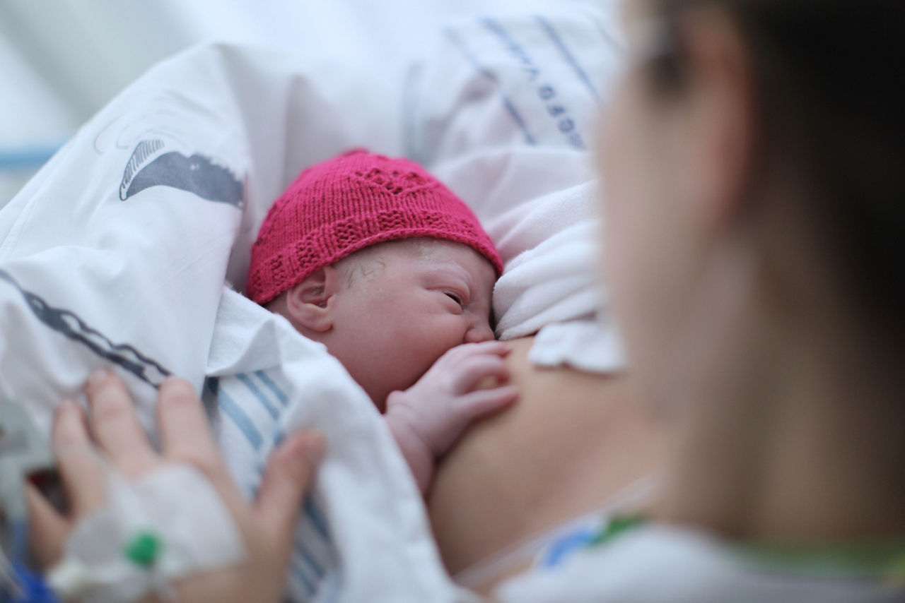 Newborn baby in pink hat breastfeeding