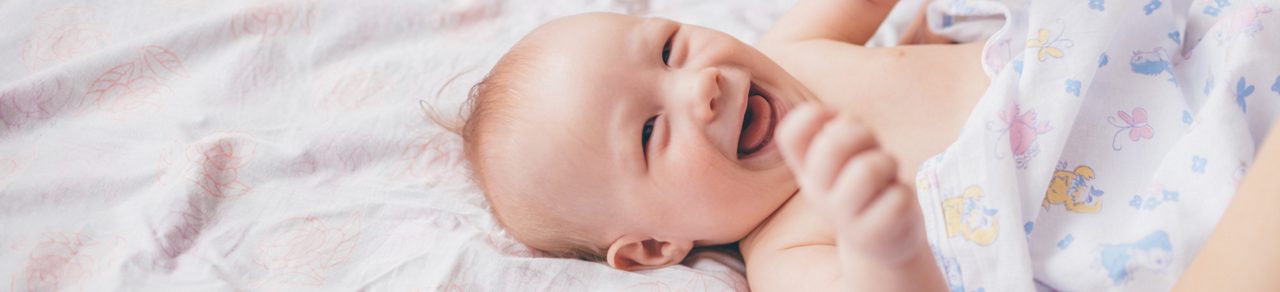 bébé riant allongé sur un drap blanc 