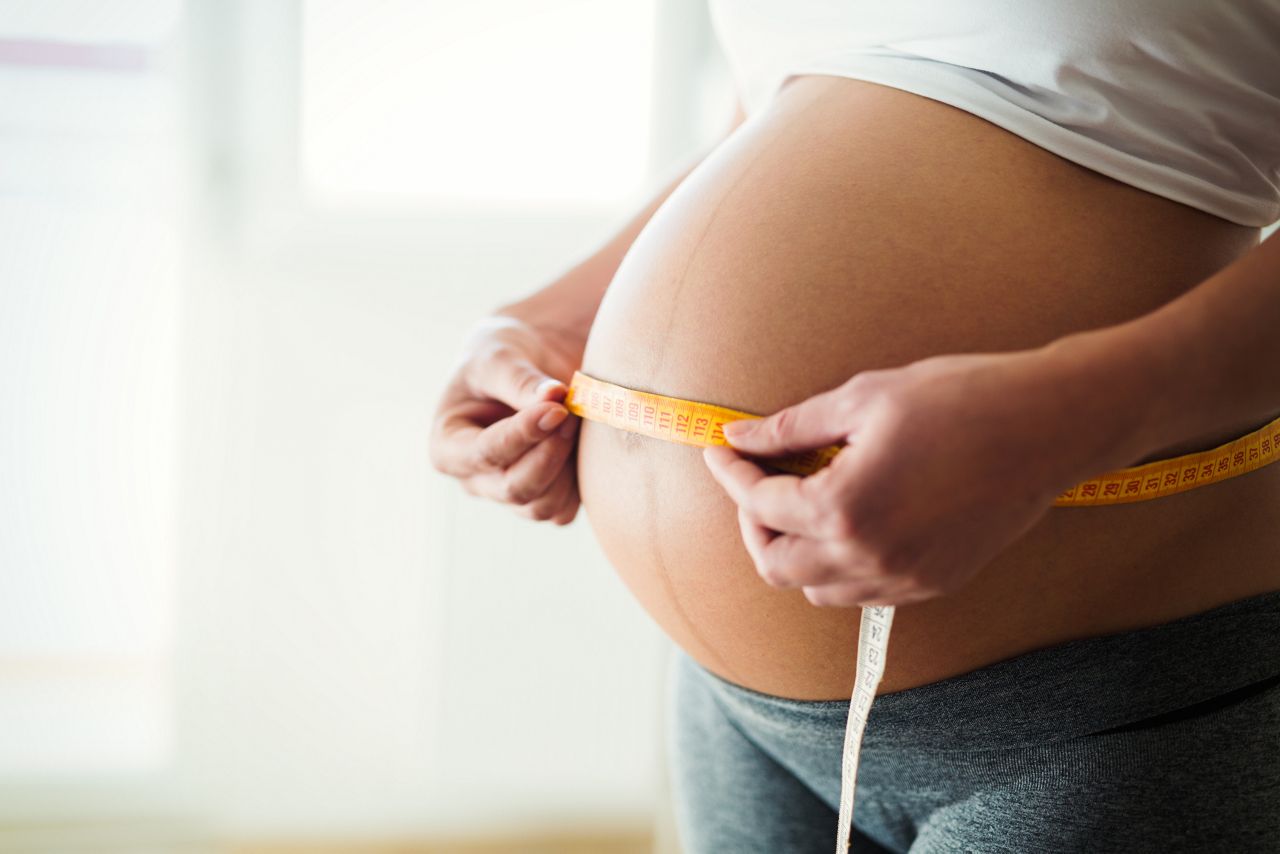 Pregnant woman measuring her stomach with measuring tape