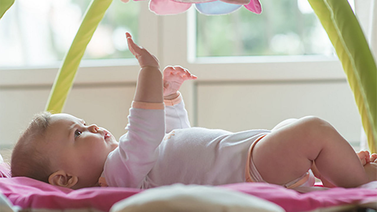 Bebé acostado jugando con un móvil, representando los signos y consejos para comenzar el destete e introducir alimentos sólidos