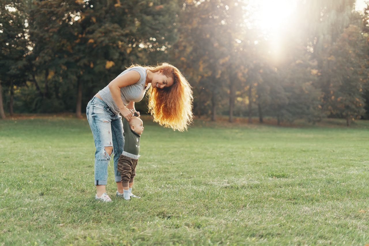 Young mother is helping her son to make first steps