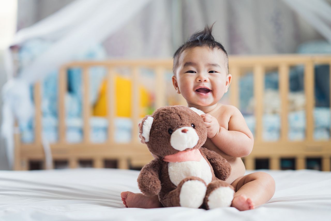 Bebe oriental em seu quarto com ursinho de pelucia