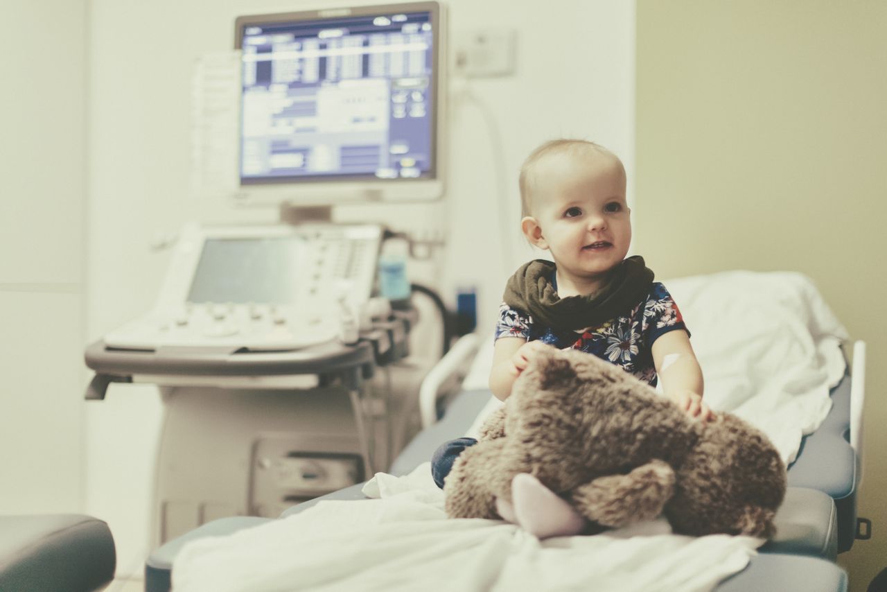 Baby girl sitting on a hospital bed, waiting for treatment.