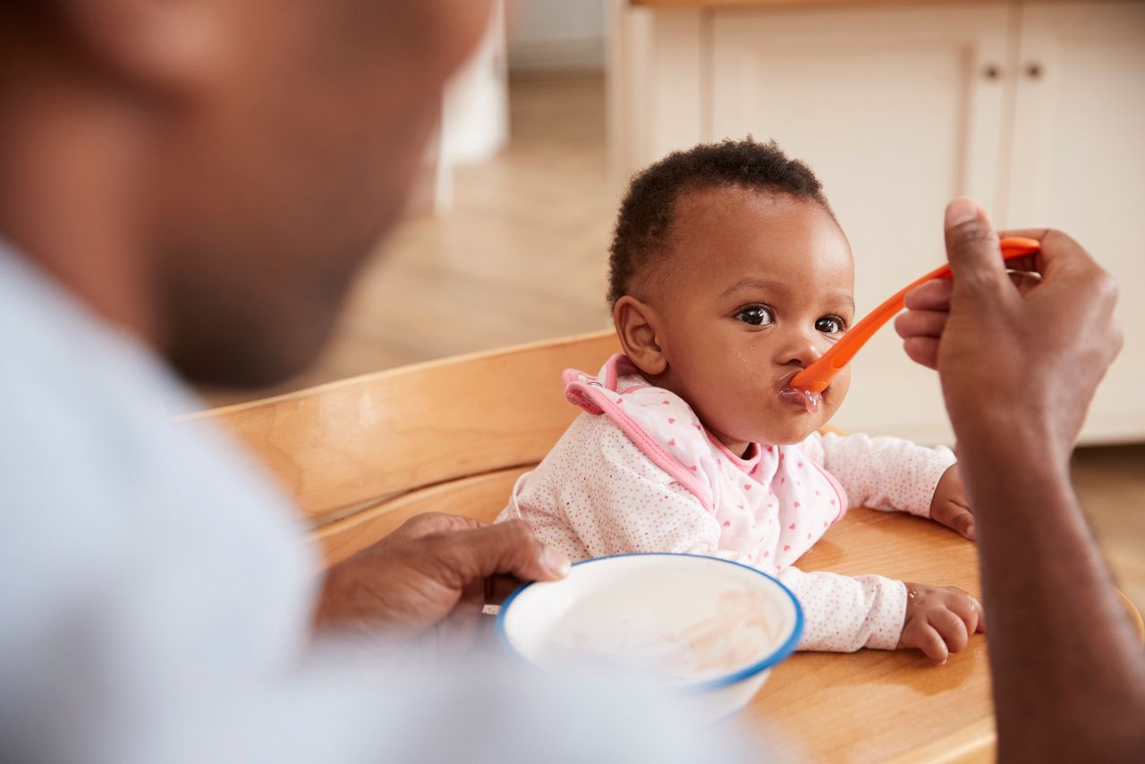 Father Feeding Baby Daughter In High Chair