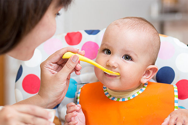 bebé con babero naranja comiendo con una cucharita