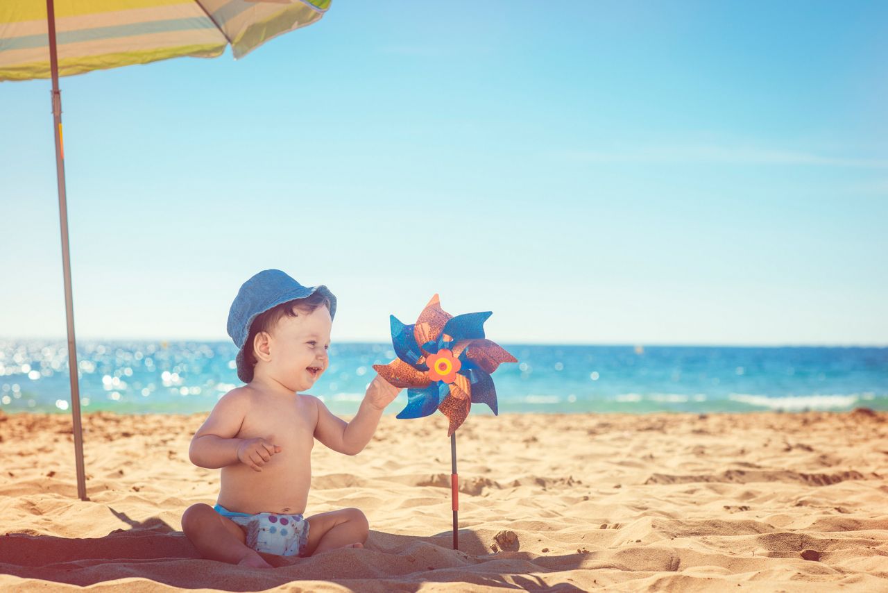 Bebe na areia da praia com chapeu e um catavento