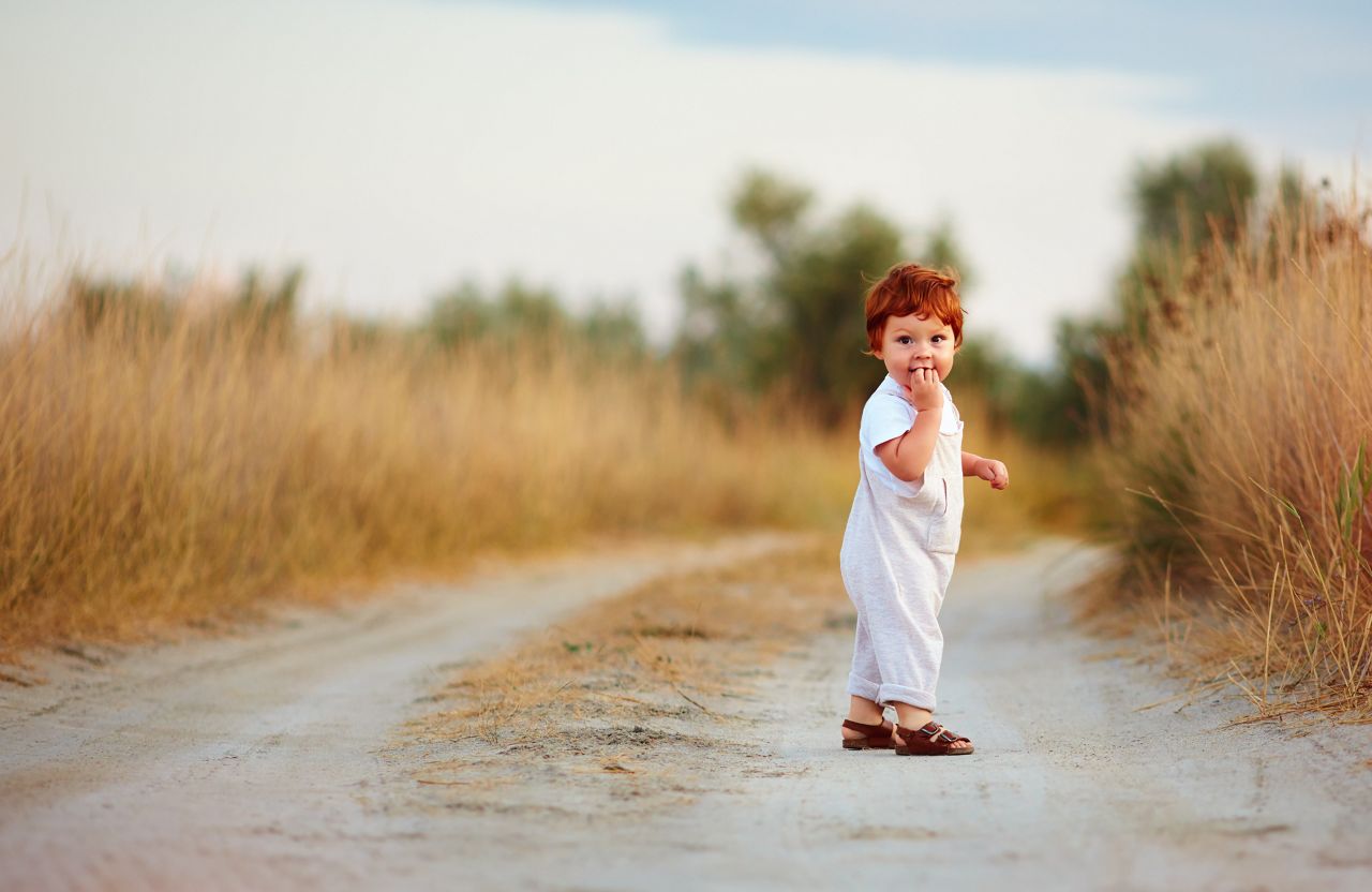 cute little redhead baby boy walking on rural path at summer day