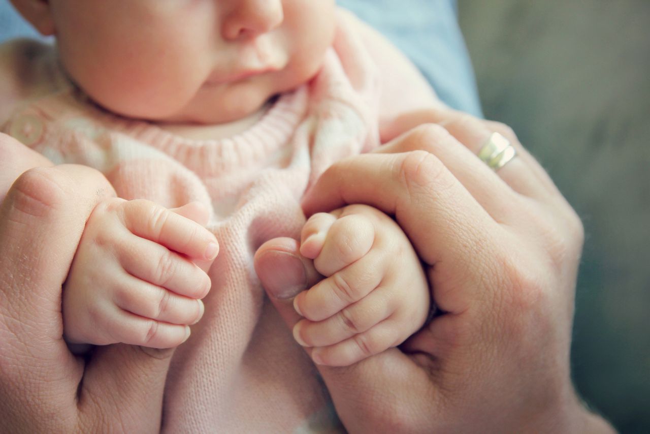 Focus on the hands of a 3 month old baby girl holding the fingers of her father.  Vintage style color filter.