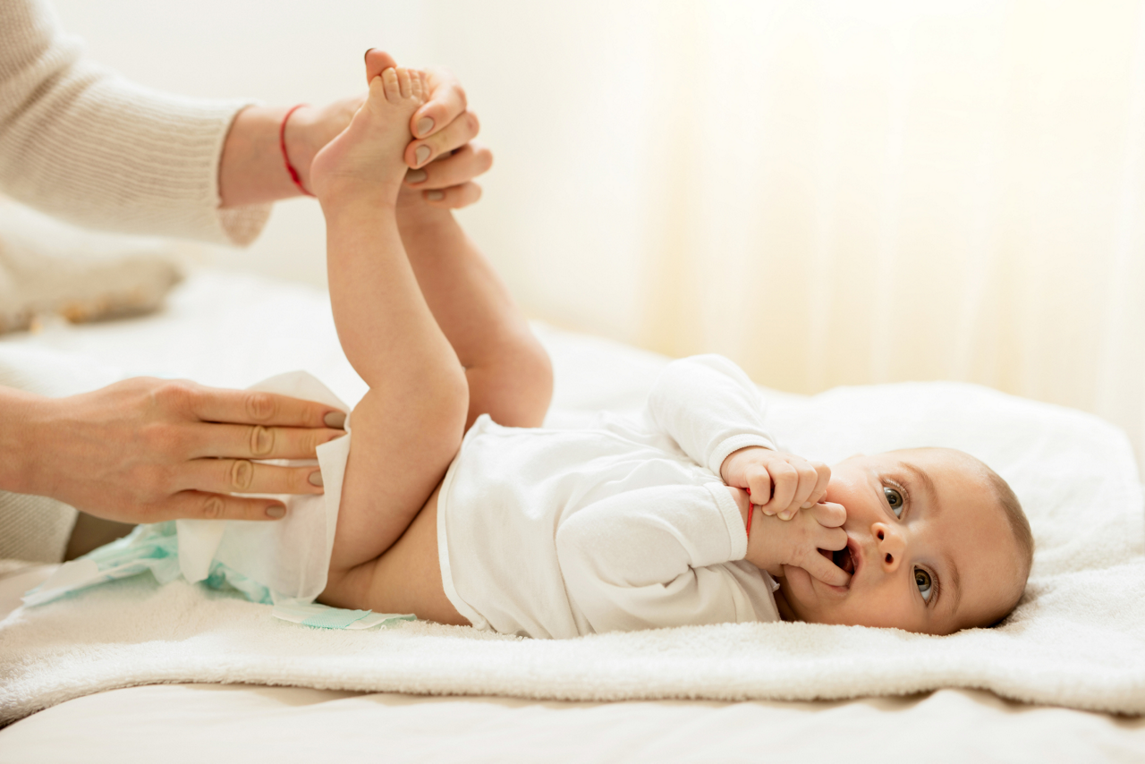 Baby boy lying on the bed with hands in the mouth while getting his diaper changed.