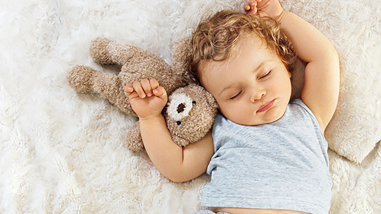 Bebe vestido de azul durmiendo con osito de peluche