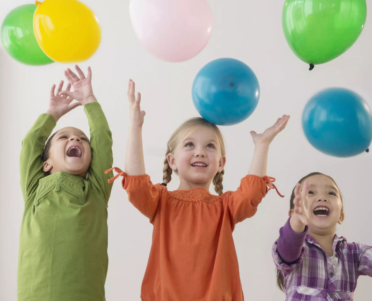 Trois enfants jouent joyeusement avec des ballons colores a l'interieur. Les ballons sont de couleurs vives, telles que le jaune, le vert, le bleu et le rose, creant une atmosphere joyeuse. Les enfants sont vetus de vetements decontractes, avec des nuances de vert, d'orange et de violet qui ajoutent a la palette vivante. L'activite capture une ambiance ludique et energique.