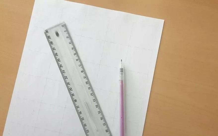 Une regle transparente et un porte-mine rose sont places sur une feuille de papier blanc avec un leger motif quadrille. Le tout est pose sur une surface en bois clair, suggerant un espace de travail ou d'etude. La regle comporte des graduations claires.