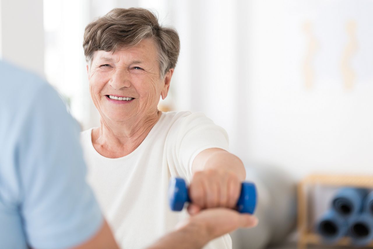 Happy senior woman exercising arms with small weights with help from a physiotherapist and copy space