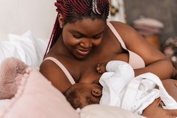 Young african american woman wearing underclothes breastfeeding her baby in bedroom