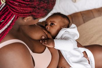 Young african american woman wearing underclothes breastfeeding her baby in bedroom