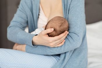 Unrecognizable Mother Holding And Breastfeeding Newborn Baby At Home, Loving Mom Tenderly Holding Head Of Her Infant Child During Lactation, Bonding With Small Kid, Closeup Shot, Cropped
