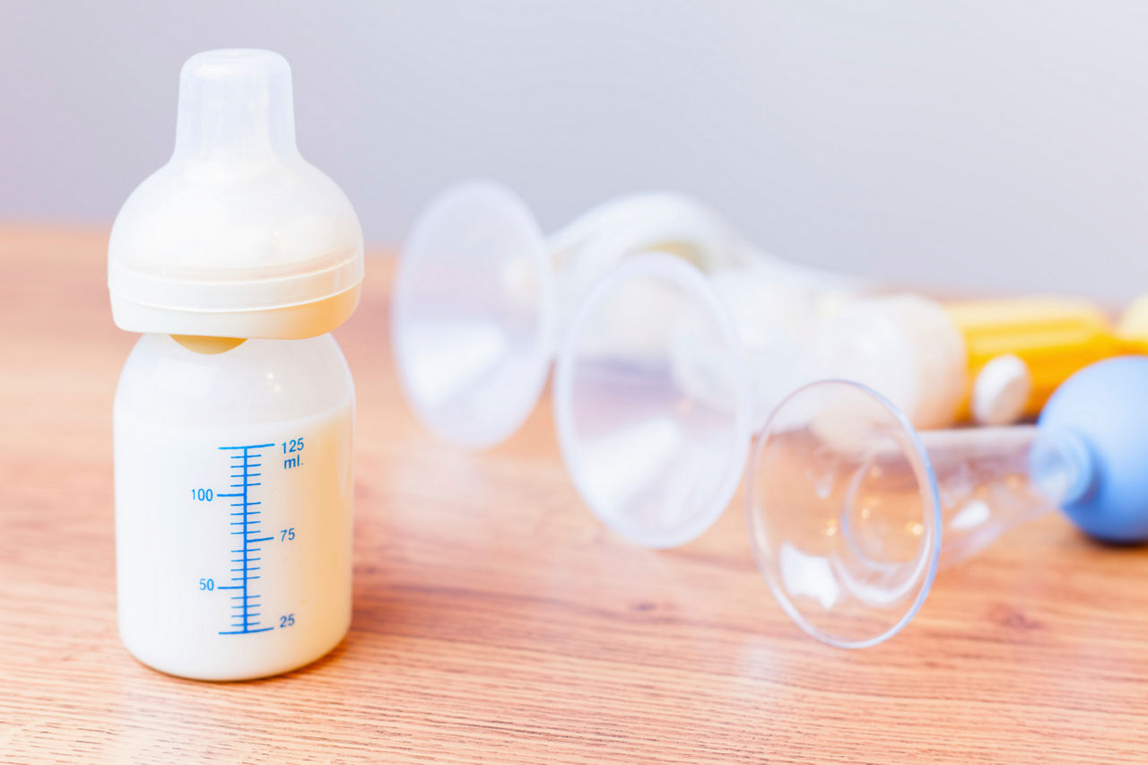 Baby bottle with milk and a measuring scale, manual breast pump, mothers breast milk is the most healthy food for newborn baby. Objects standing in a row. Selective focus
