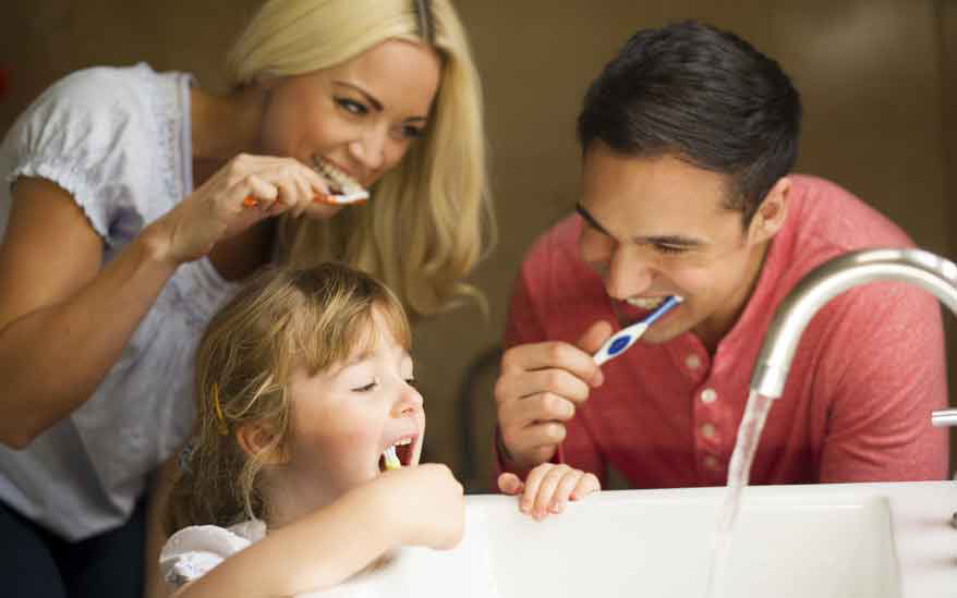 Une famille se rassemble autour du lavabo de la salle de bain pour se brosser les dents ensemble. Le decor comprend un robinet ouvert et un environnement familial decontracte. La scene met l'accent sur les routines d'hygiene quotidiennes et les moments de complicite familiale.