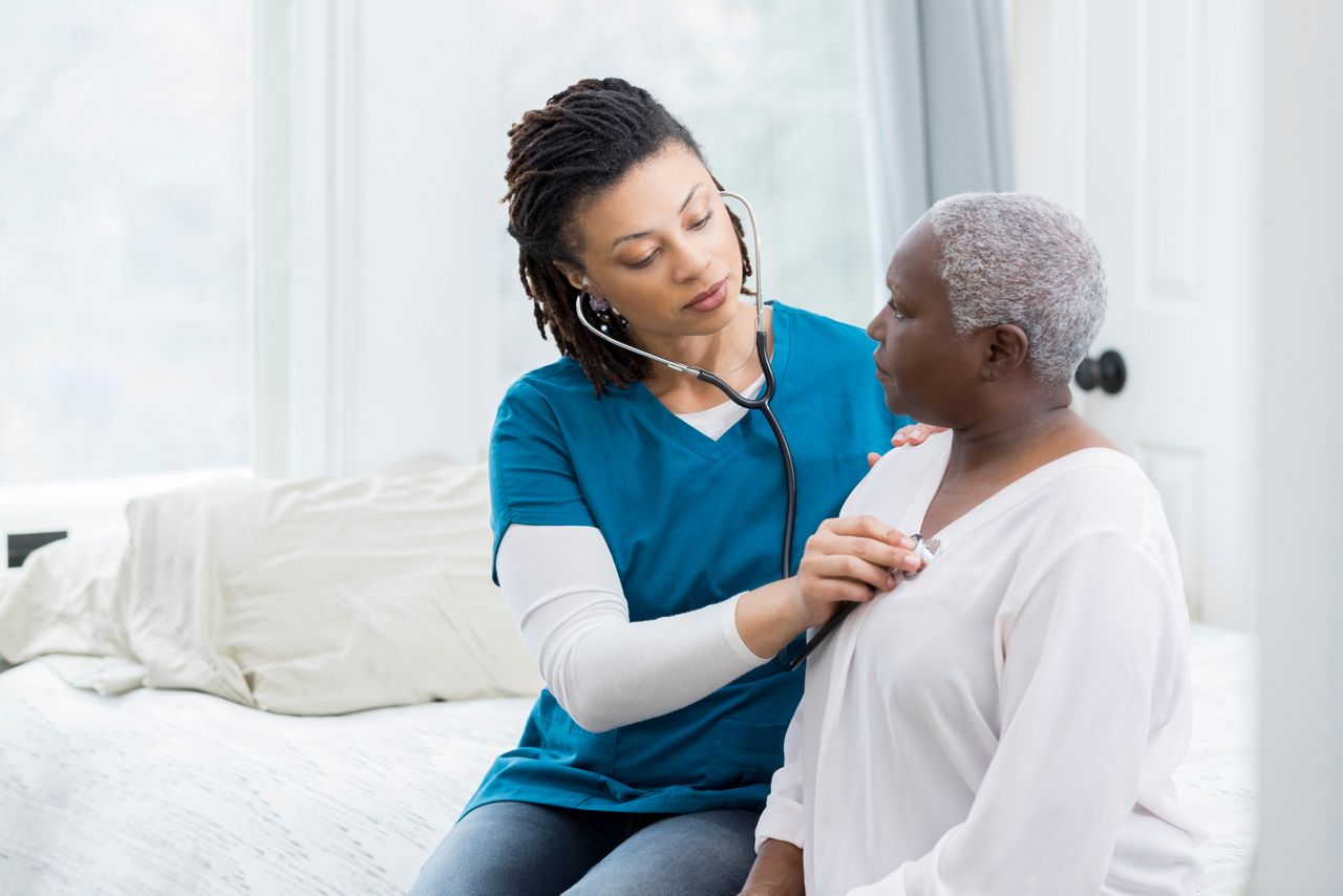 Mid adult female nurse concentrates while listening to an elderly female patients heart and lungs during exam.